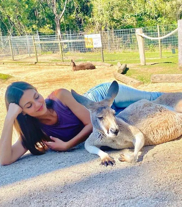 Žena leží vedľa klokana v prírodnej rezervácii na slnku, s úsmevom sledujú okolie.