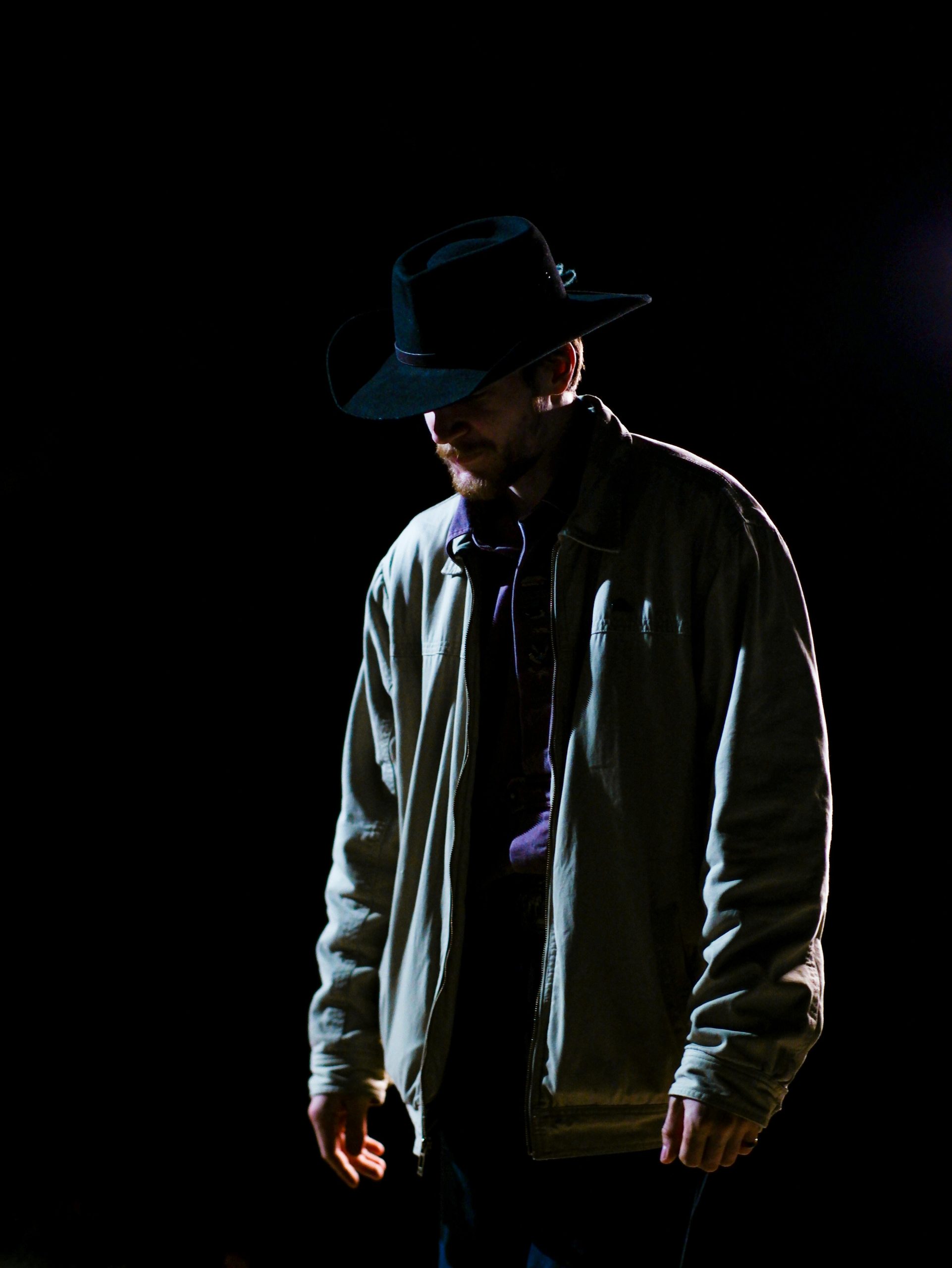 Osoba v klobúku a bunde osvetlená v tme. Mysteriózna atmosféra noci.