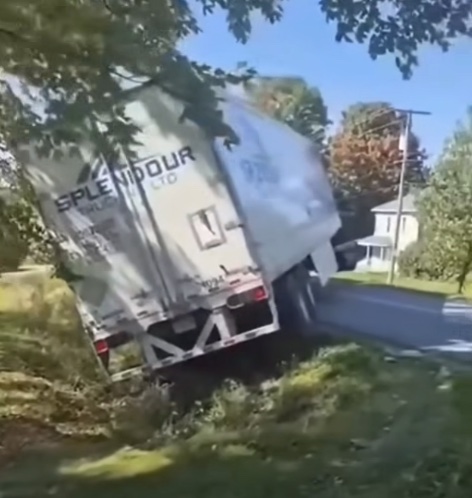 Kamión uviazol v priekopu pri ceste, obklopený stromami, na slnečný deň.