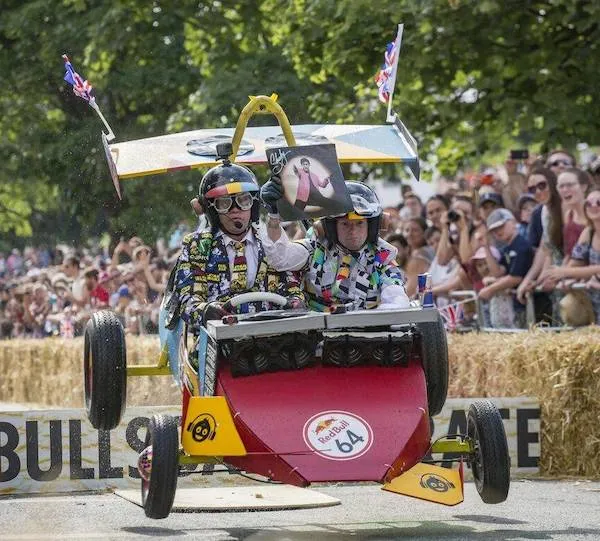 Preteky kreatívnych vozidiel na Red Bull podujatí, vozidlo číslo 64 vo vzduchu, veľký dav divákov.