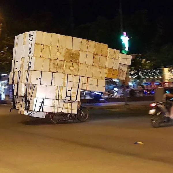 Motorka preplnená krabicami jazdí v noci po ceste, nebezpečne preťažená nákladom.