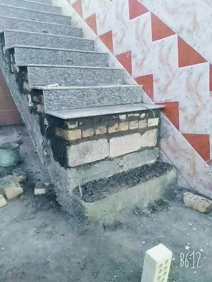 Nedokončené schodisko s odkrytými tehlami a dlaždicami na stene, znaky konštrukčných prác.