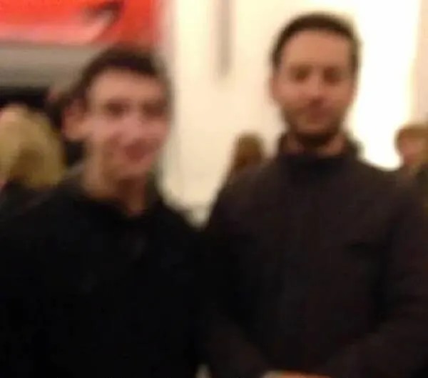 Dvaja ľudia stojaci v rozmazanom prostredí, pozadie s červeným detailom.