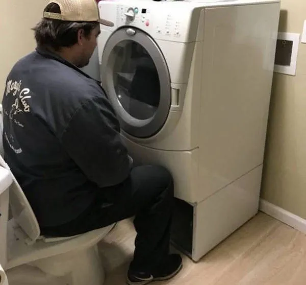 Muž na toalete sedí oproti práčke v kúpeľni, netradičné riešenie priestoru.