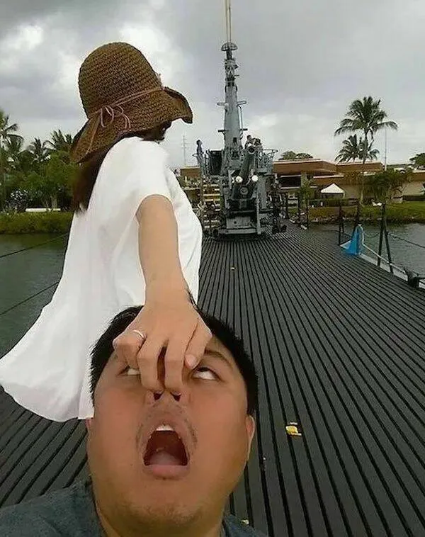 Osoba vtipne ťahá inú za nos na lodi, pozadie tvorí palmy a mraky.