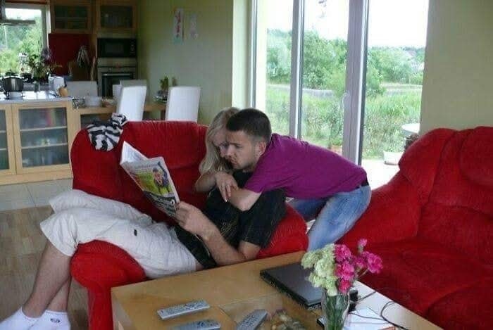 Muž na červenej pohovke číta časopis, zatiaľ čo ho objíma žena v obývačke s výhľadom do záhrady.