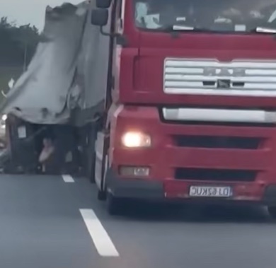 Červený kamión s poškodeným nákladným priestorom na diaľnici počas dňa.