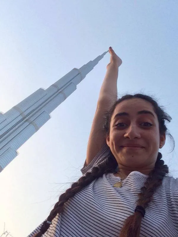 Osoba s vrkočmi sa fotí pred mrakodrapom Burj Khalifa v Dubaji, ukazujúc na jeho špičku.