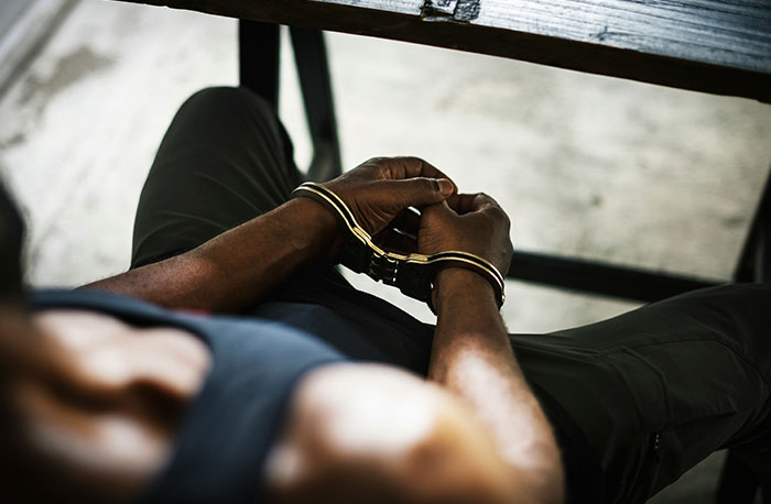 Osoba so zloženými rukami v putách sediaca pri stole, pohľad zhora.