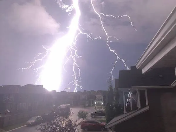 Blesk osvetľuje nočnú oblohu nad mestskou štvrťou počas letnej búrky, zachytávajúc silu prírody.