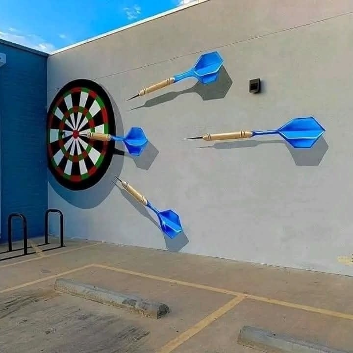 3D nástenná maľba s terčom a letiacimi šípkami na bielej budove, vytvára realistický efekt.