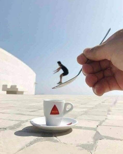 Optická ilúzia s človekom na lyžičke, ktorá sa chystá skočiť do šálky kávy na slnečnej terase.