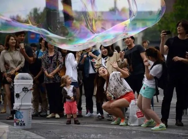 Skupina ľudí s nadšením sleduje obrovskú bublinu na verejnej akcii v parku.