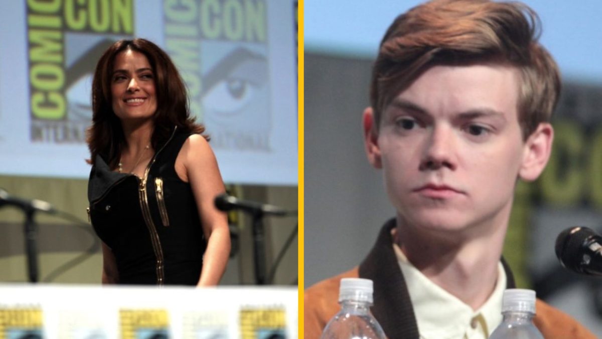 Dvojica ľudí na konferencii Comic Con, diskutujú pred publikom s logom Comic Con v pozadí.