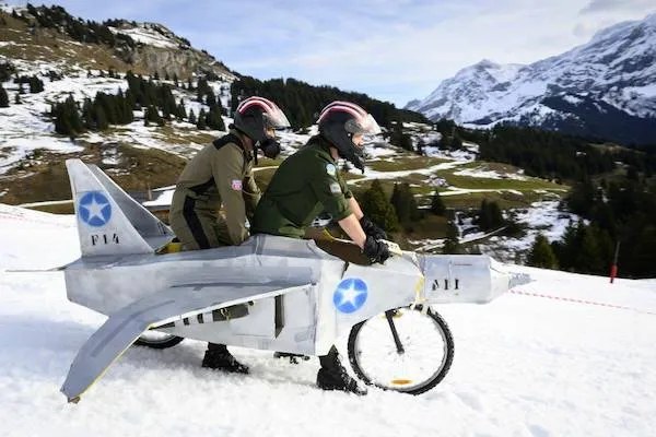 Ľudia na bicykli v tvare lietadla na zasneženej horskej ceste.
