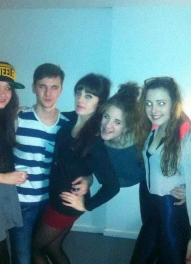 Skupina piatich mladých ľudí sa baví na večierku, všetci usmiati a objímajúci sa v priateľskej atmosfére.