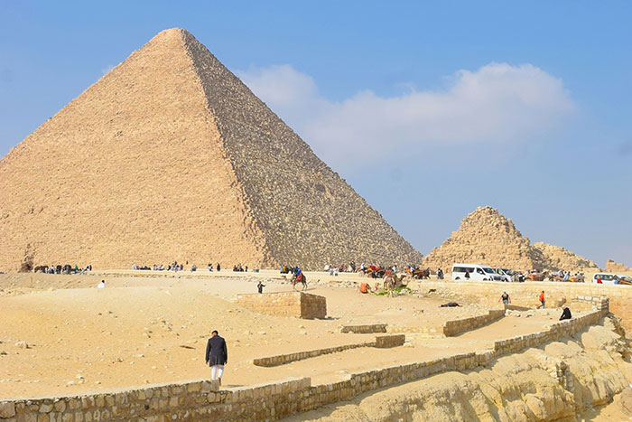 Veľká pyramída v Gíze pod modrou oblohou, s turistami a autobusmi v popredí. Historické miesto v Egypte.