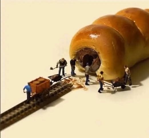 Miniatúrni robotníci stavajú chodník do chleba, pripomínajúci tunelovú výstavbu. Kreatívna scénka zo života.