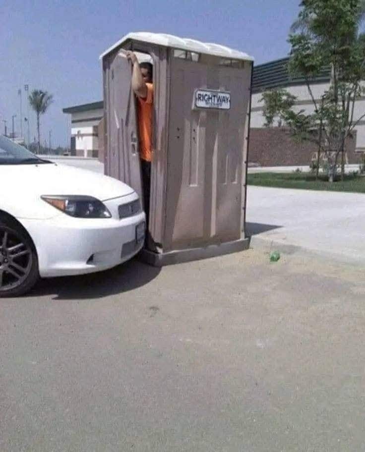 Auto zaparkované tesne pri prenosnej toalete, muž vychádza dverami.