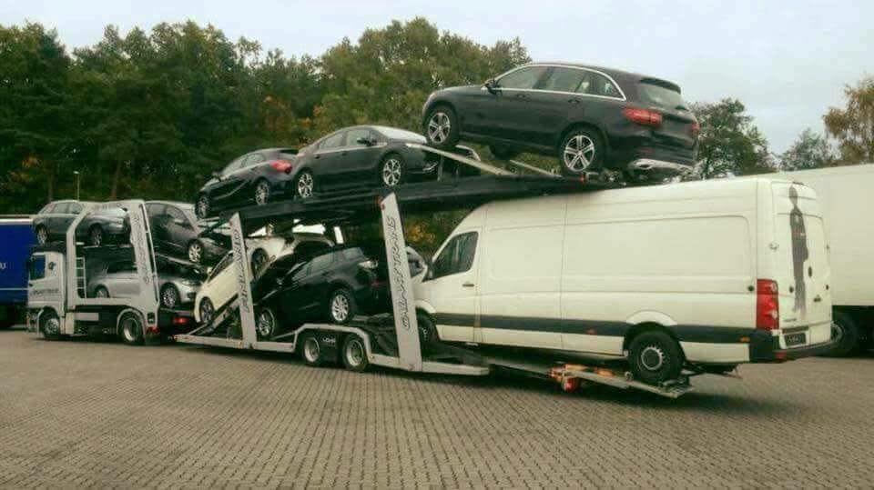 Preprava áut na plošinovom kamióne s dodávkou na ceste, parkovaná na odpočívadle pri lese.