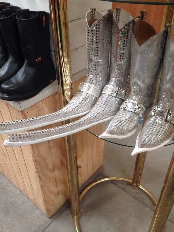 Strieborné kožené topánky s dlhými špicmi vystavené v obchode, vedľa čiernych čižiem.