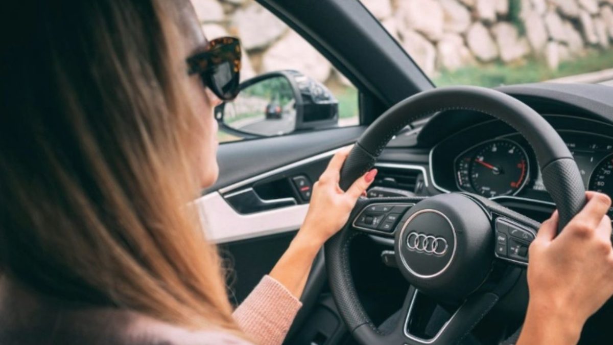 Žena šoféruje auto značky Audi, drží volant, oblečená v svetri a má na sebe slnečné okuliare.