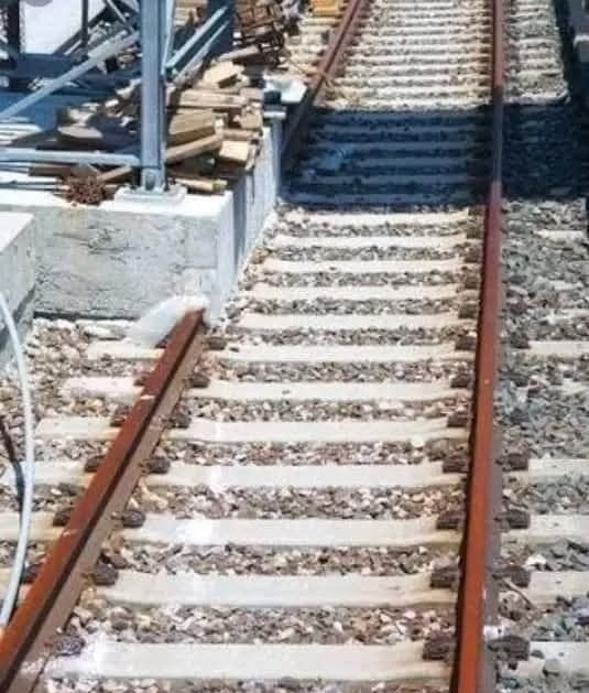 Železničná trať končiaca na platforme so stavebnými materiálmi, znázornujúca nedokončenú železničnú stavbu.