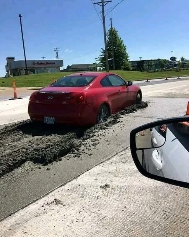 Červené auto uviazlo v mokrom betóne na ceste počas dňa.