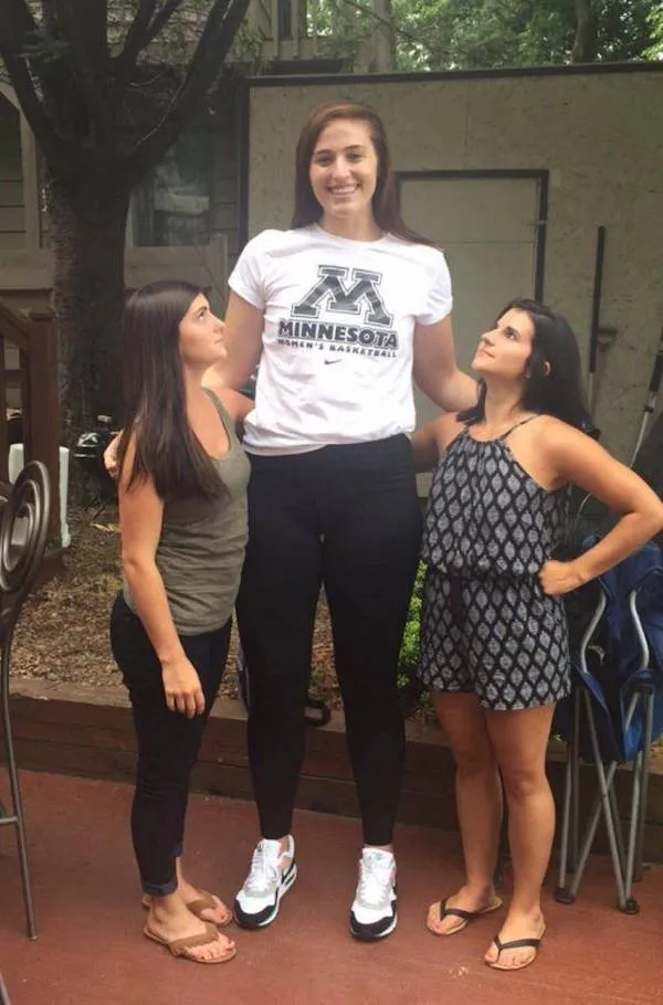 Žena v tričku Minnesota stojí medzi dvoma menšími ženami, všetky sa usmievajú v záhradnom prostredí.