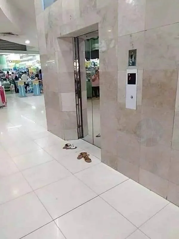 Opustené sandále pred otvoreným výťahom v nákupnom centre.