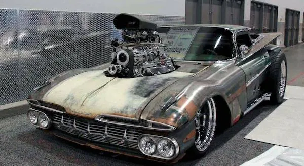 Svalnatý historický automobil s viditeľným motorom vystavený na autosalóne v interiéri haly.