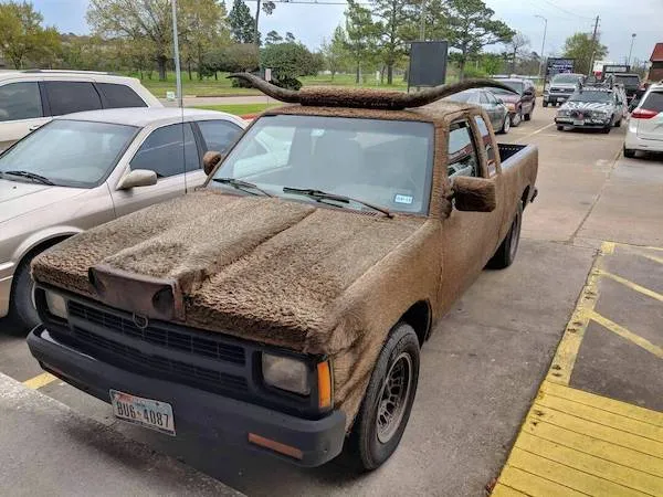 Auto pokryté chlpatým koberecom s rohmi na kapote stojace na parkovisku.