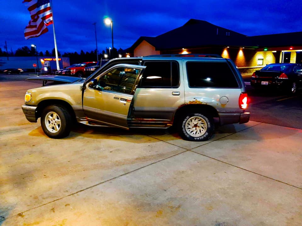 SUV s otvorenými dverami na parkovisku, večerná atmosféra, americká zástava veje v pozadí.