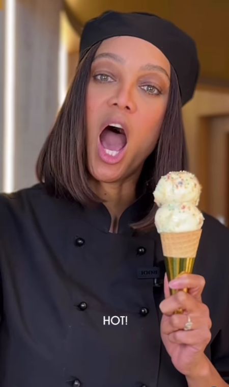 Osoba v kuchárskej zástere drží zmrzlinový kornútok s dvoma kopčekmi, vyzerá prekvapene.