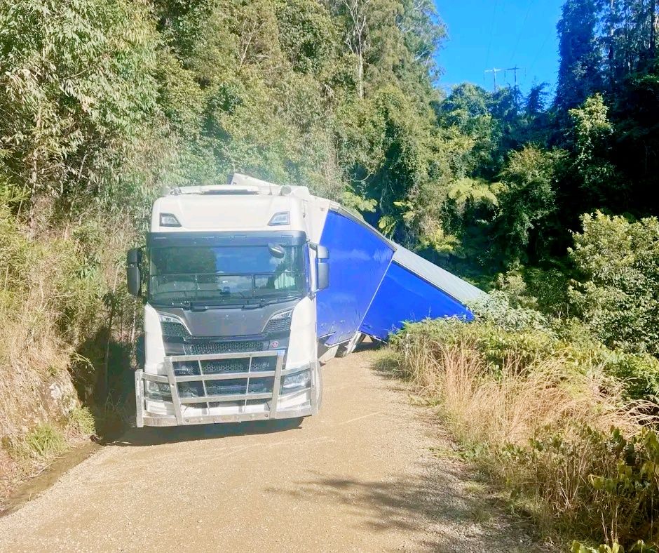 Kamión uviazol na úzkej lesnej ceste, nákladiak je naklonený do priekopy vedľa cesty obklopenej hustou zeleňou.