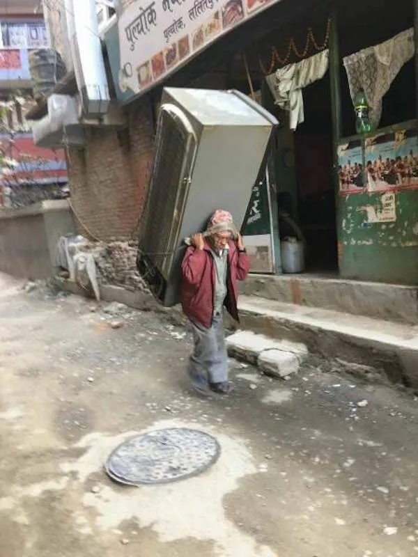 Muž nesie na chrbte veľkú chladničku po ulici plnej obchodov v meste.