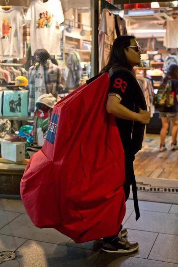 Osoba nesúca nadrozmerný červený ruksak pred obchodom s oblečením.