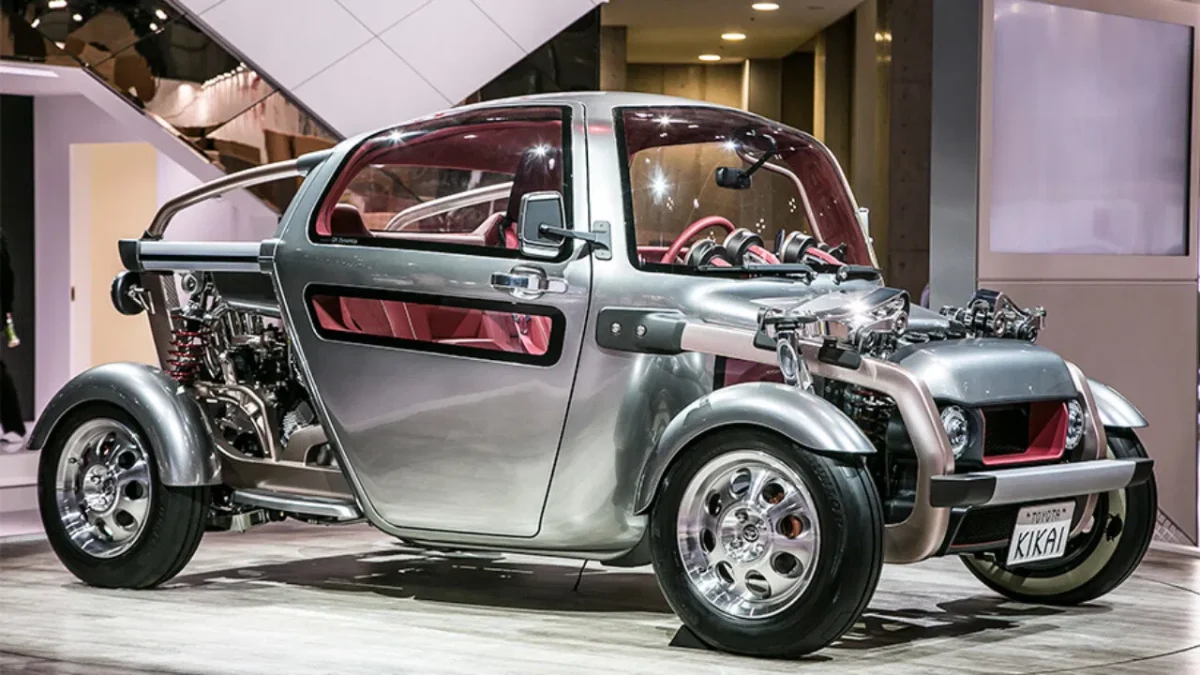 Inovatívne futuristické auto s otvorenou konštrukciou na výstave, strieborný exteriér a červený interiér.