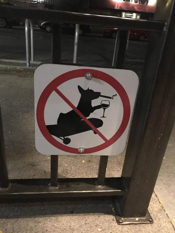 Zákaz jazdy na skateboarde so psom, vínom a cigaretou - zábavná zákazová značka na ulici.