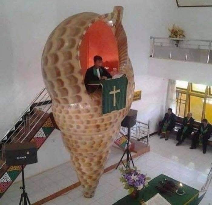 Kazateľ hovorí z kazateľnice v tvare obrovskej ulitovej špirály v modernej kostolnej sále.