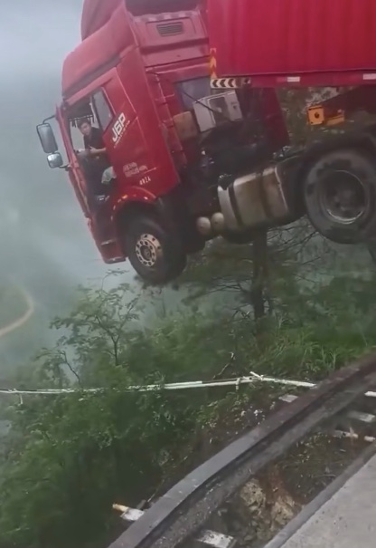 Kamión balansujúci na okraji cesty v hornatej oblasti, vodič v kabíne, dramatická situácia nad priepasťou.