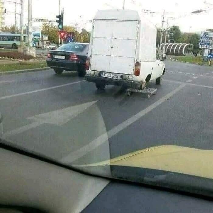 Dodávka s provizórnym náhradným kolesom na vozíčku na križovatke v meste.