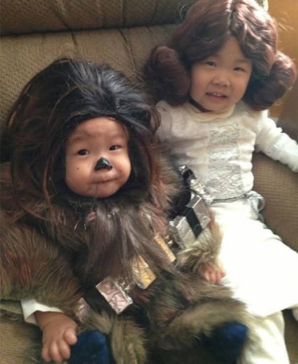 Dve deti oblečené v kostýmoch z Hvězdnych válek, jedna ako Chewbacca a druhá ako princezná Leia, sedia na pohovke.
