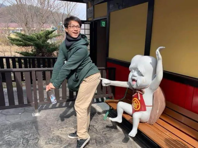 Osoba pózuje so sochou na lavičke, ktorá na ňu gestikuluje v humornom prostredí.