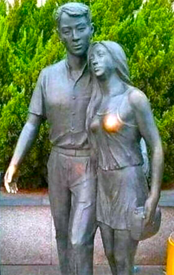 Socha muža a ženy v objatí na pozadí zelene.