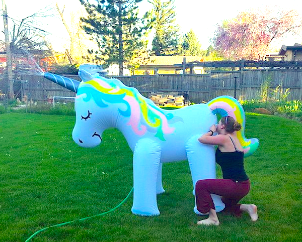 Osoba nafukuje veľkého farebného nafukovacieho jednorožca na záhrade.