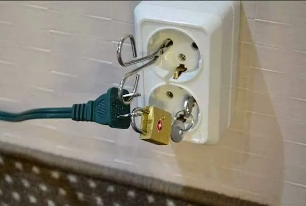 Elektrická zásuvka s visiacim zámkom a zapojeným káblom, netradičné riešenie ochrany elektrického pripojenia.