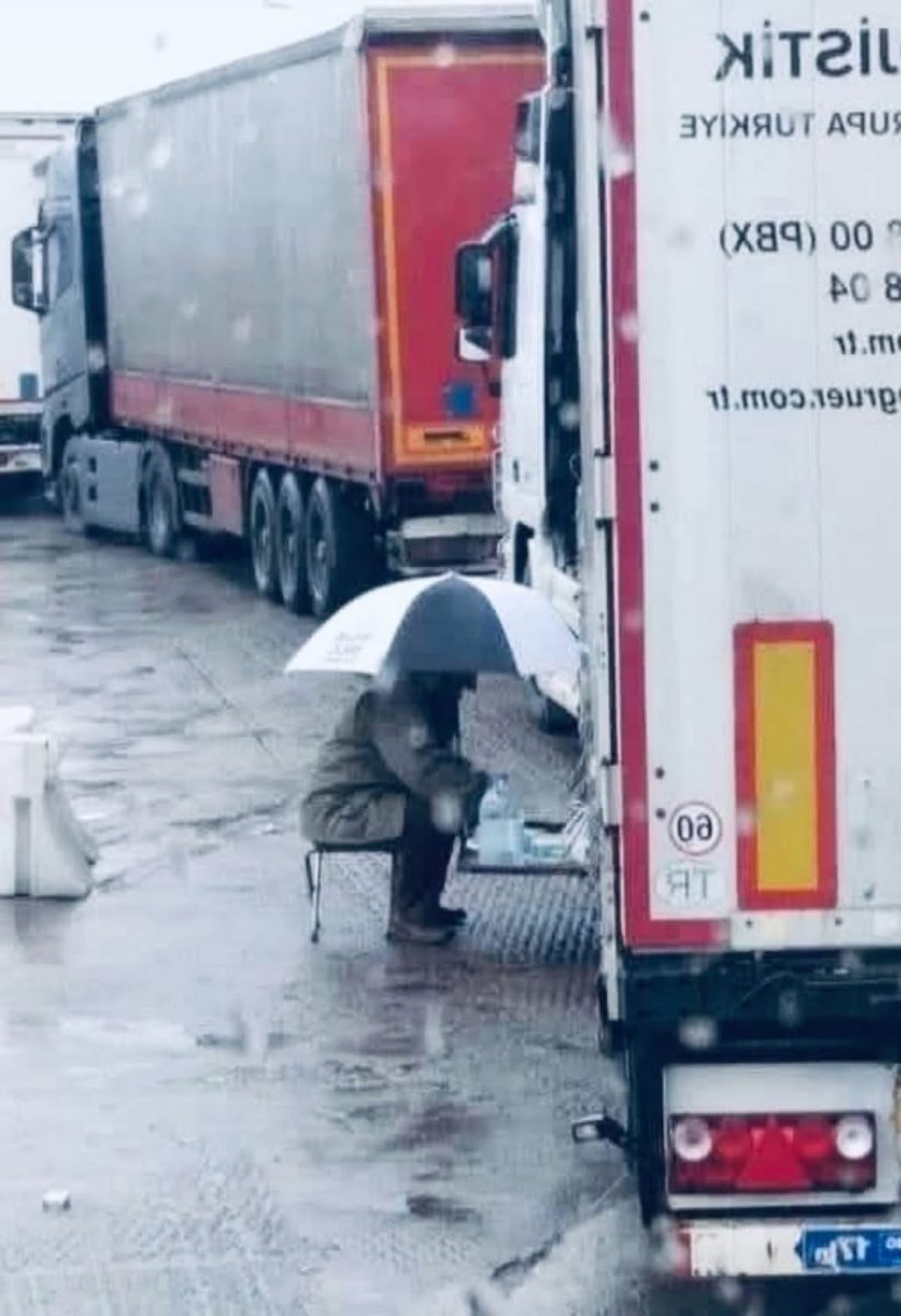 Osoba pod dáždnikom sedí na stoličke vedľa kamiónu v daždivom počasí.