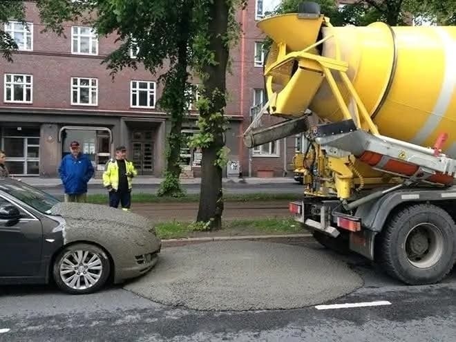 Auto zasypané betónom z miešačky na ulici, dvaja muži situáciu sledujú.