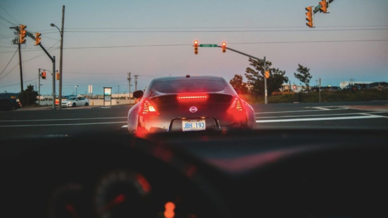 Auto na semafore počas súmraku, pohľad z predného sedadla druhej auta; rozsvietené brzdové svetlá.